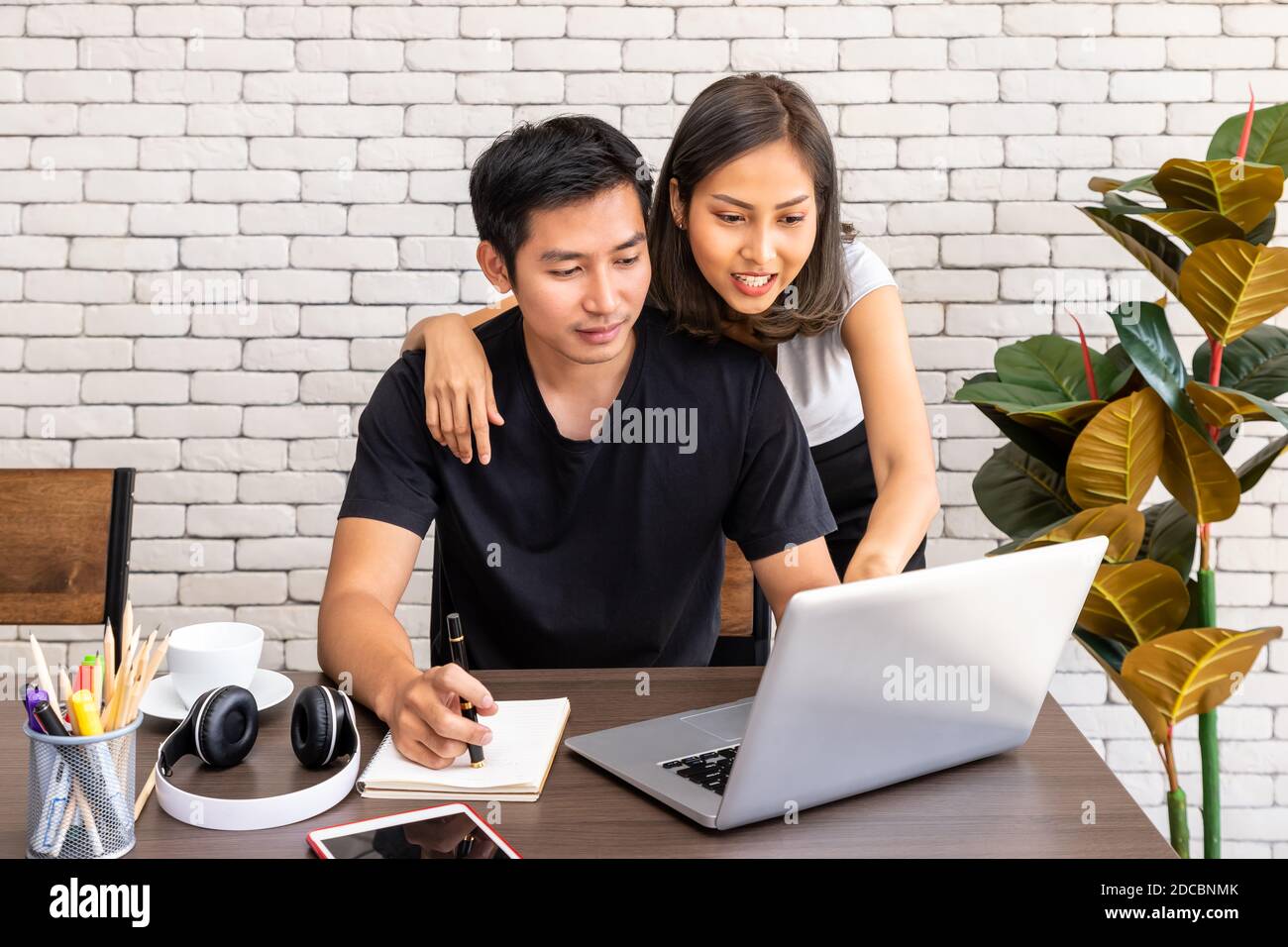 Donna asiatica moglie motivare consiglio uomo marito freelancer lavorare a casa, seduto al tavolo da pranzo scrivania in soggiorno Foto Stock