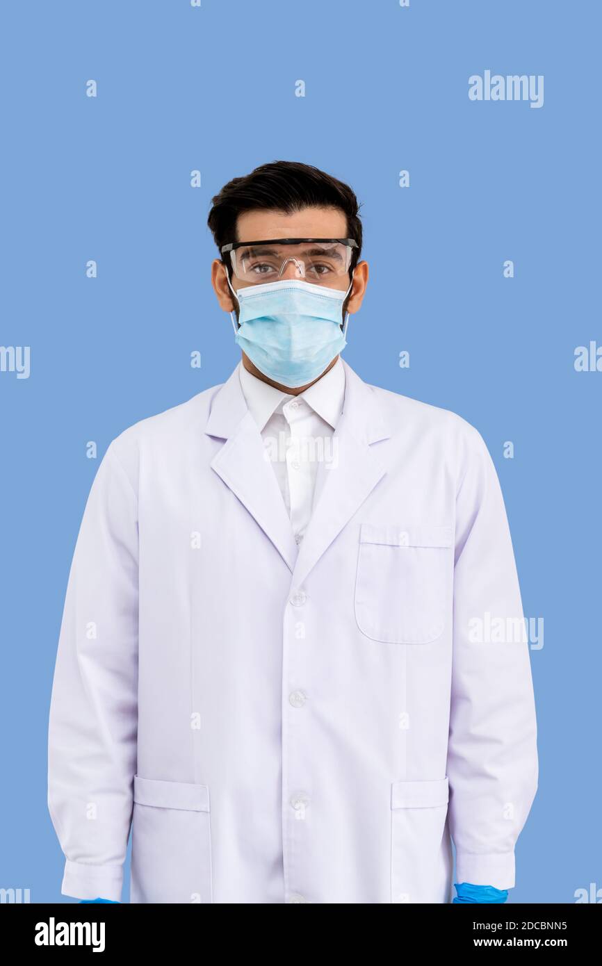 Ritratto di sicuro ricercatore arabo medio orientale maschile scienziato medico medico indossando maschera chirurgica e occhiali di protezione in piedi isolati Foto Stock
