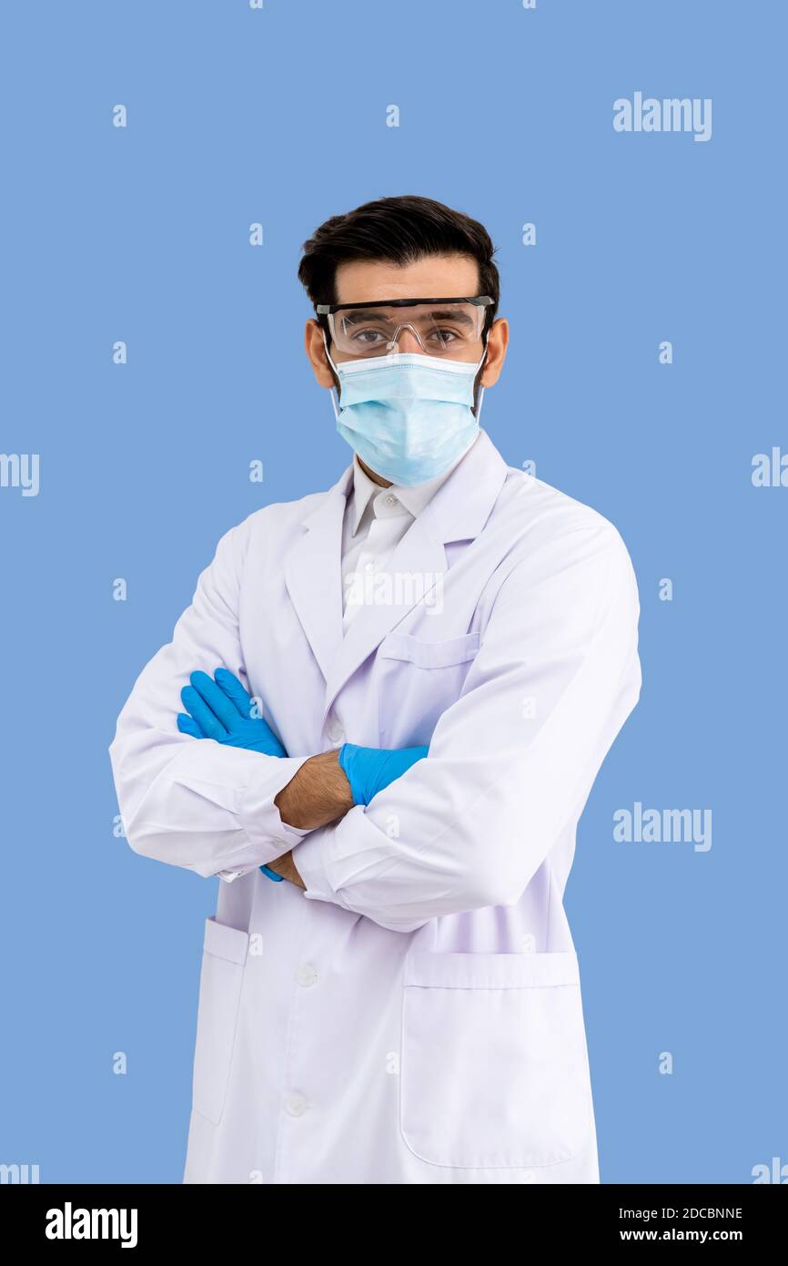 Ritratto di sicuro ricercatore arabo medio orientale maschile scienziato medico medico che indossa maschera chirurgica e occhiali di protezione in piedi braccia trasversali è Foto Stock