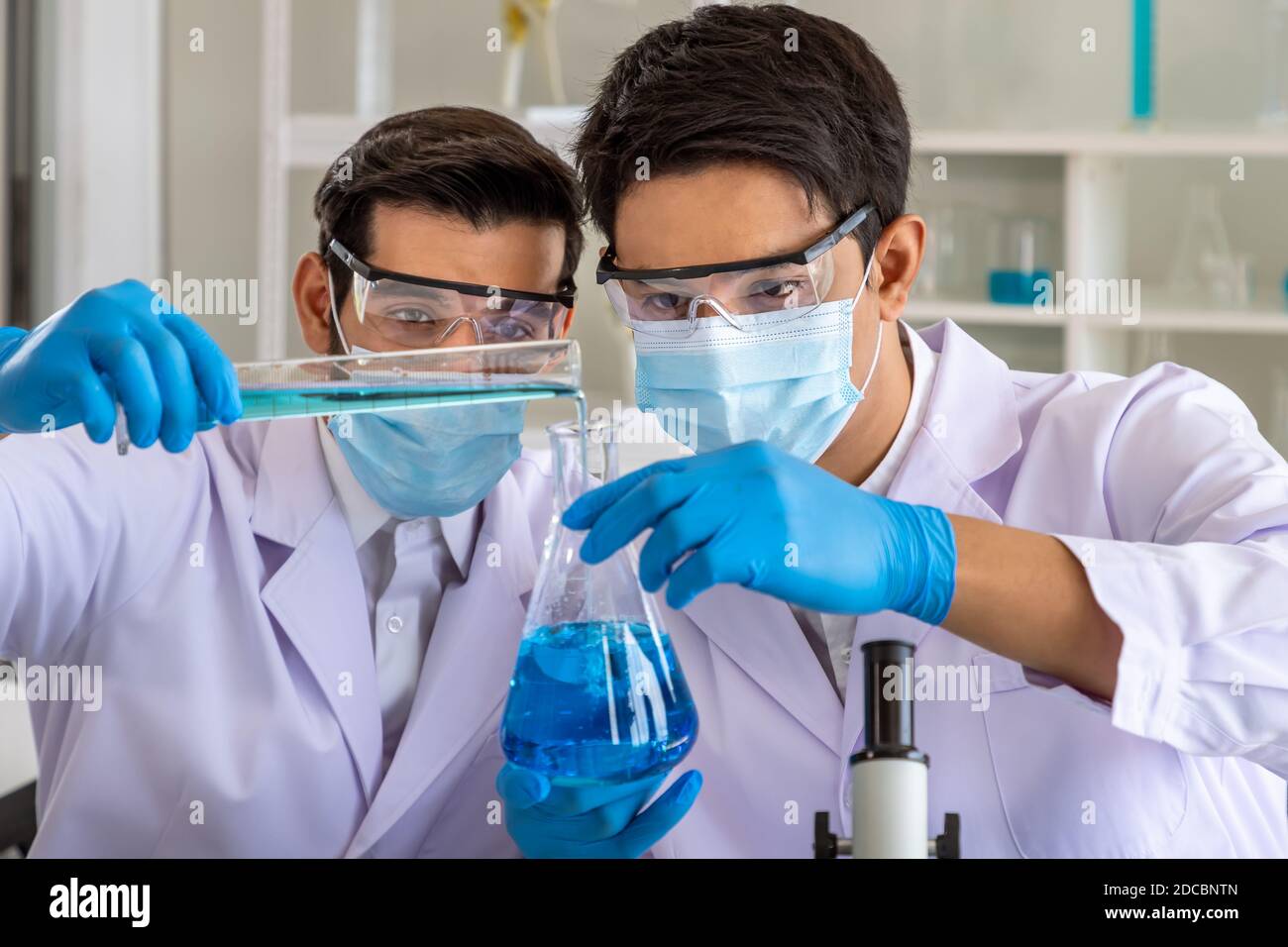 Due ricercatori asiatici e arabi maschi che lavorano in laboratorio, conducendo studio sostanza a rischio biologico con apparecchiature scientifiche e microscopio Foto Stock