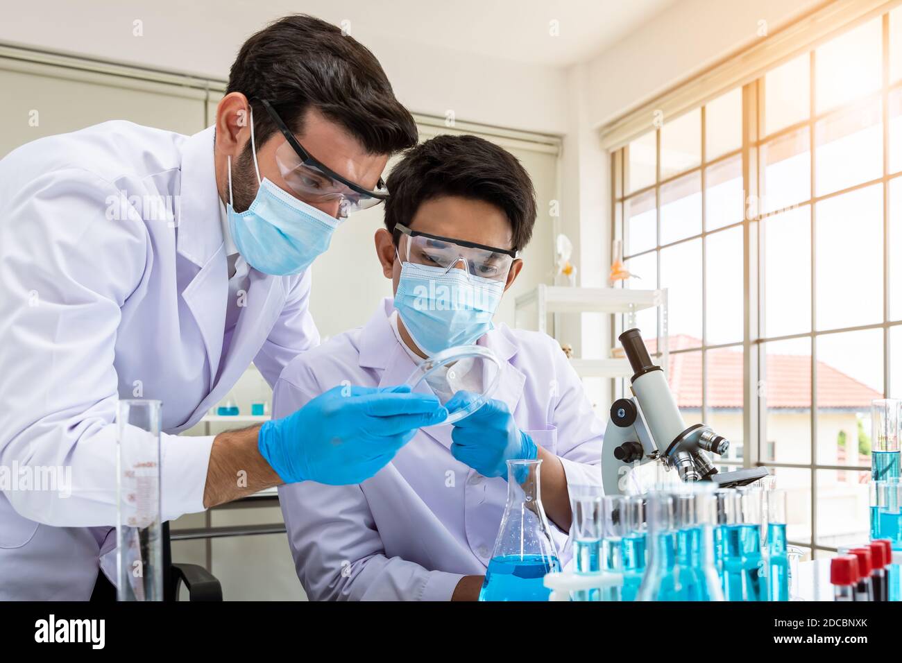 Due ricercatori asiatici e arabi maschi che lavorano in laboratorio, conducendo studio sostanza a rischio biologico con apparecchiature scientifiche e microscopio Foto Stock