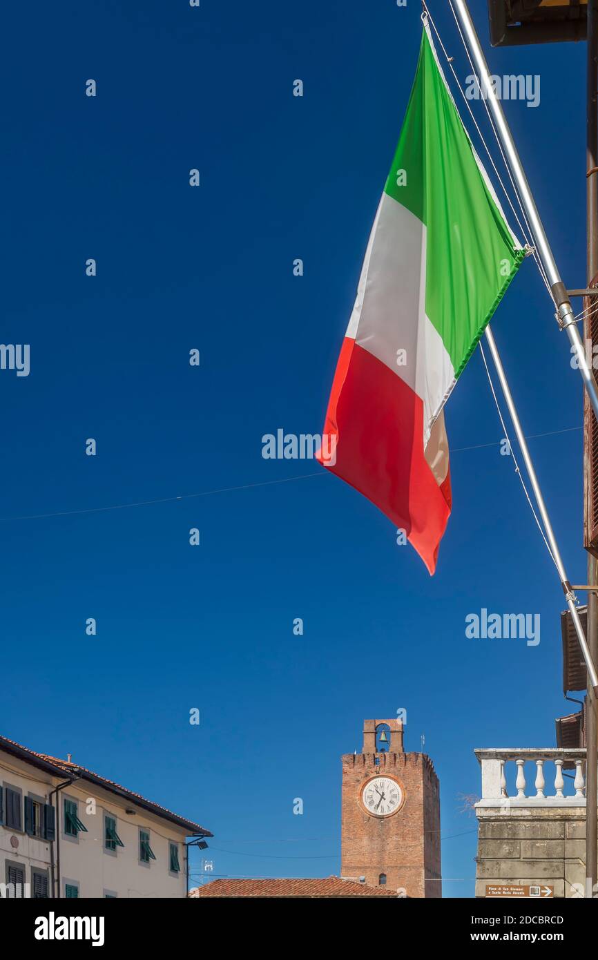 Vista verticale della strada principale del centro storico di Cascina, Pisa, Italia, con la bandiera italiana e la torre dell'orologio in una giornata di sole Foto Stock