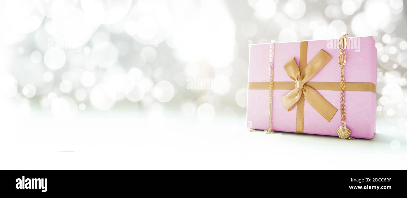Scatola regalo rosa con nastro d'oro e decorazioni d'oro. Sfondo bokeh. Vista laterale. Spazio di copia. Foto Stock