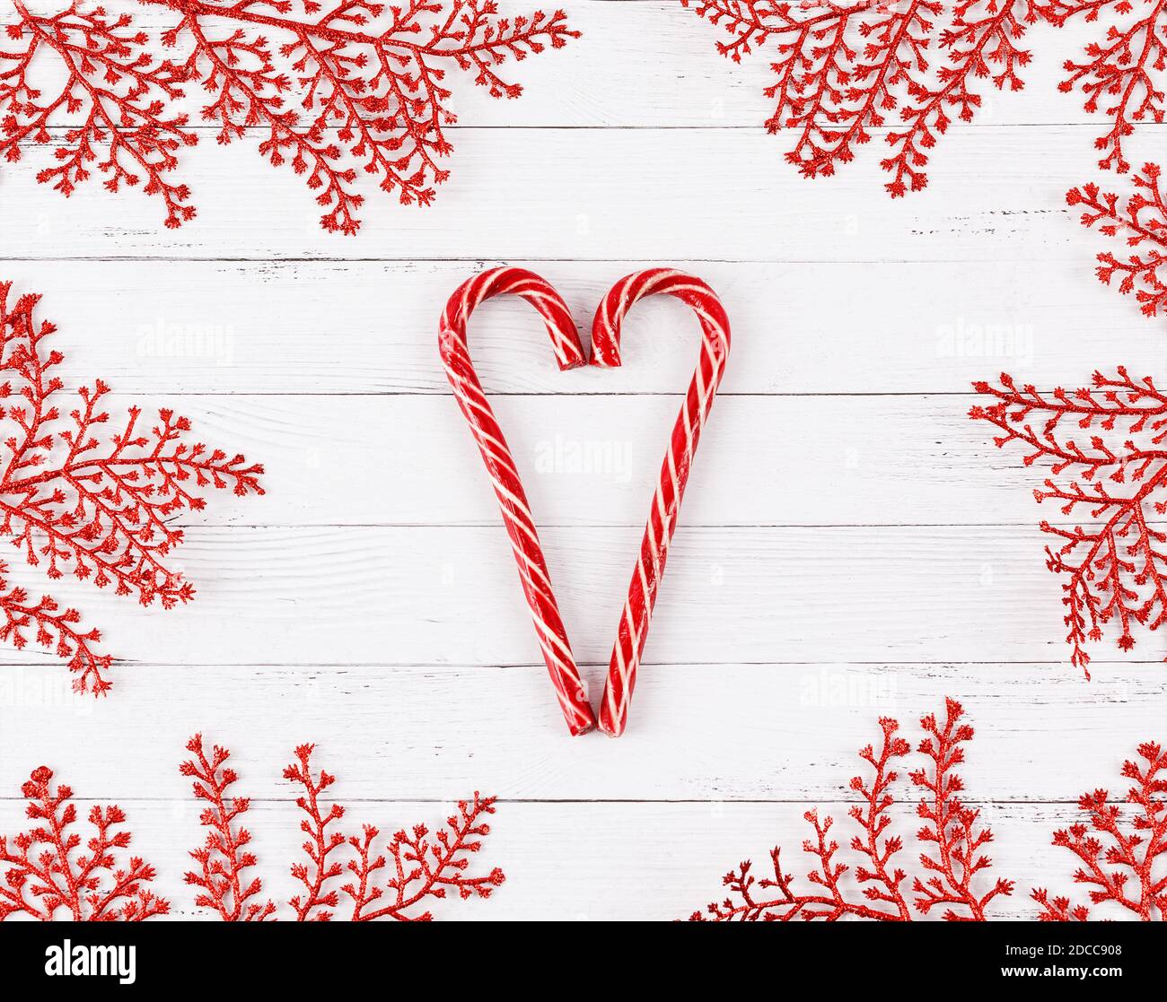 Forma a cuore fatta di canne caramelle su tavole di legno bianche con rametti di glitter rosso incorniciati. Concetto di Natale. Foto Stock