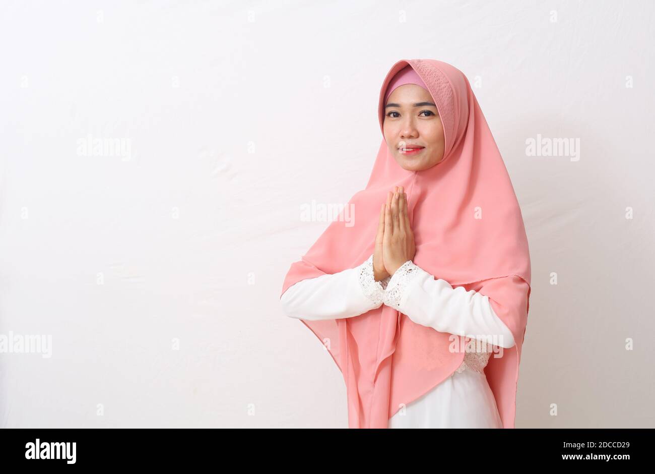 Una donna asiatica in abito musulmano si alza in una posa verde per le mani di Namaste, accogliendo gli ospiti, IED Fitr saluto. Isolato su sfondo bianco Foto Stock