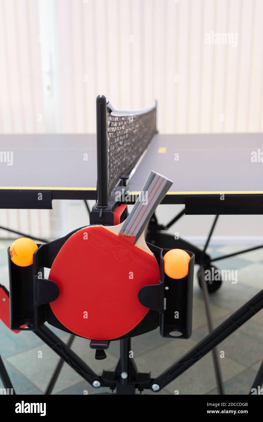 Vista laterale di un tavolo da ping-pong e di una rete con un pipistrello da ping pong rosso e due tavoli arancioni palle da tennis in un supporto Foto Stock