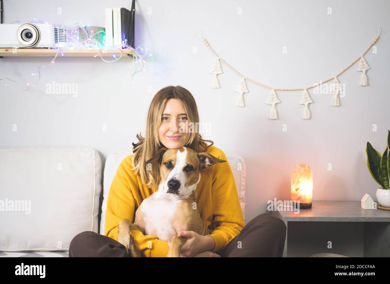 Ritratto di una donna felice con il suo cane terrier staffordshire. Gioia da animali domestici a casa o durante il blocco o l'isolamento, freddo stagione invernale Foto Stock