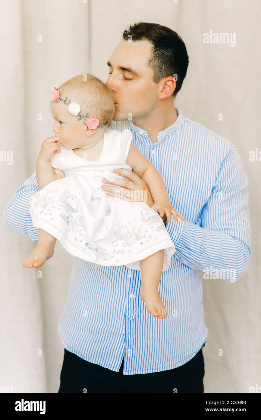 Il padre felice tiene e bacia la sua bambina in abito con la corona sulla sua testa. Foto Stock