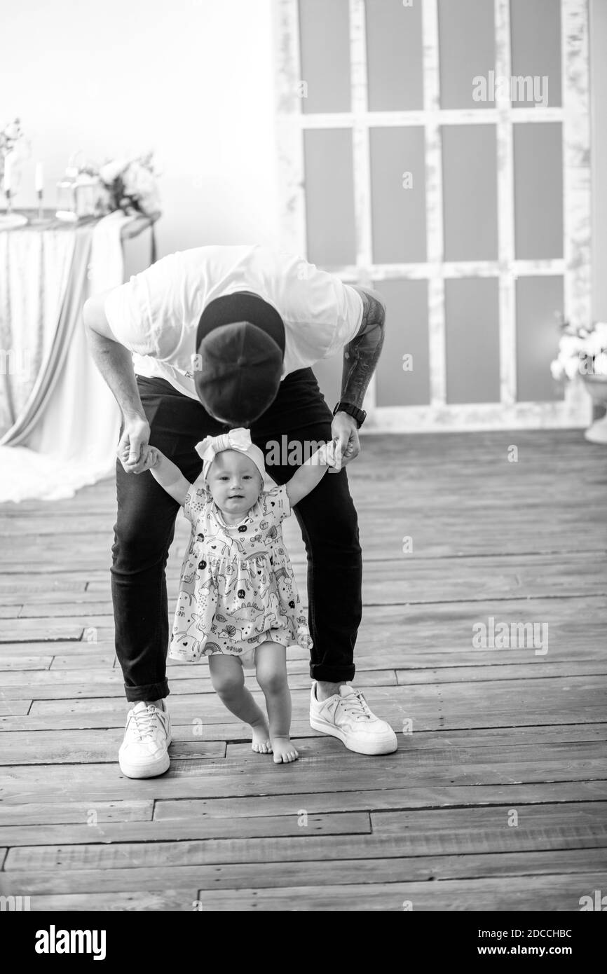 Il giovane padre insegna a camminare e conduce per le mani la sua piccola figlia. Immagine in bianco e nero. Foto Stock