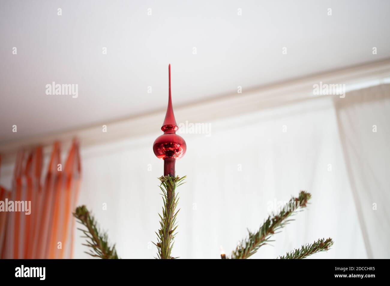 Albero di Natale decorato, vero abete Nordmann di fronte alla camera offuscata con tende arancioni. Un albero rosso decorativo e molto spazio vuoto. Insolito Foto Stock
