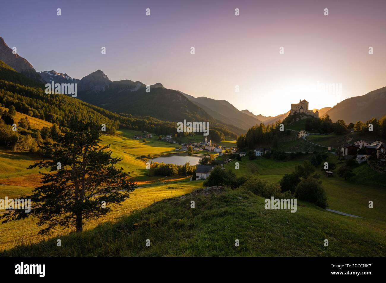 Il sole sorge sulle montagne che circondano Tarasp e il suo castello, nel cantone di Graubünden (Engadin) Svizzera. Foto Stock
