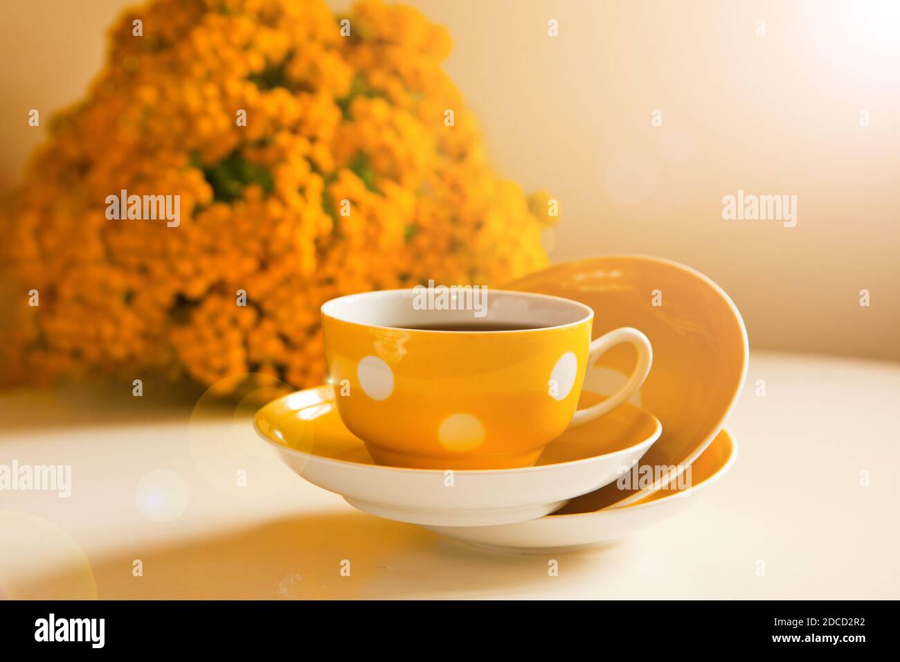 tazze da caffè gialle volanti su sfondo bianco, pausa caffè e dipendenza da caffeina. fiori gialli sul tavolo. luce chiara in camera Foto Stock