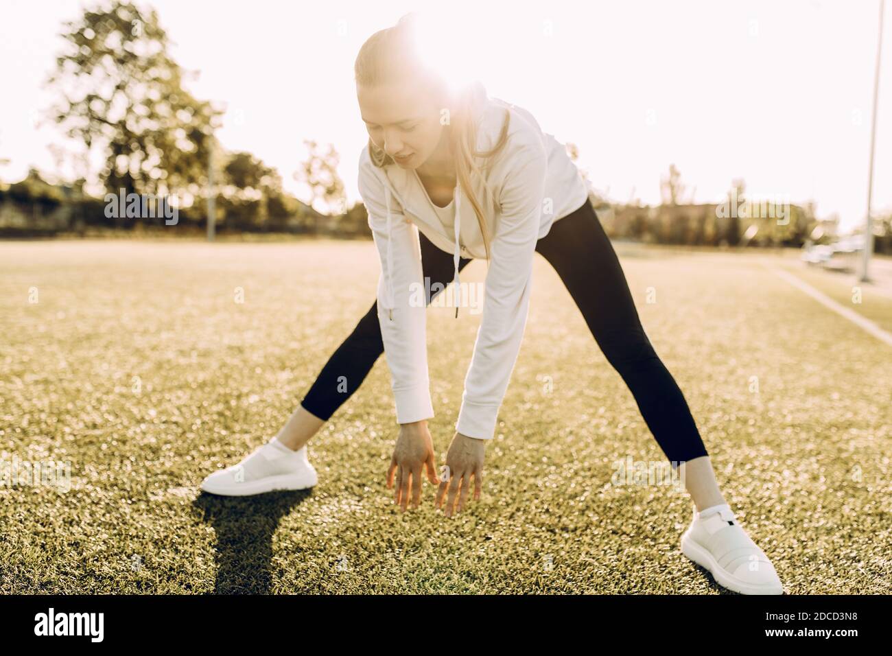 Atleta snella in abiti sportivi, facendo stretching al mattino all'alba Foto Stock