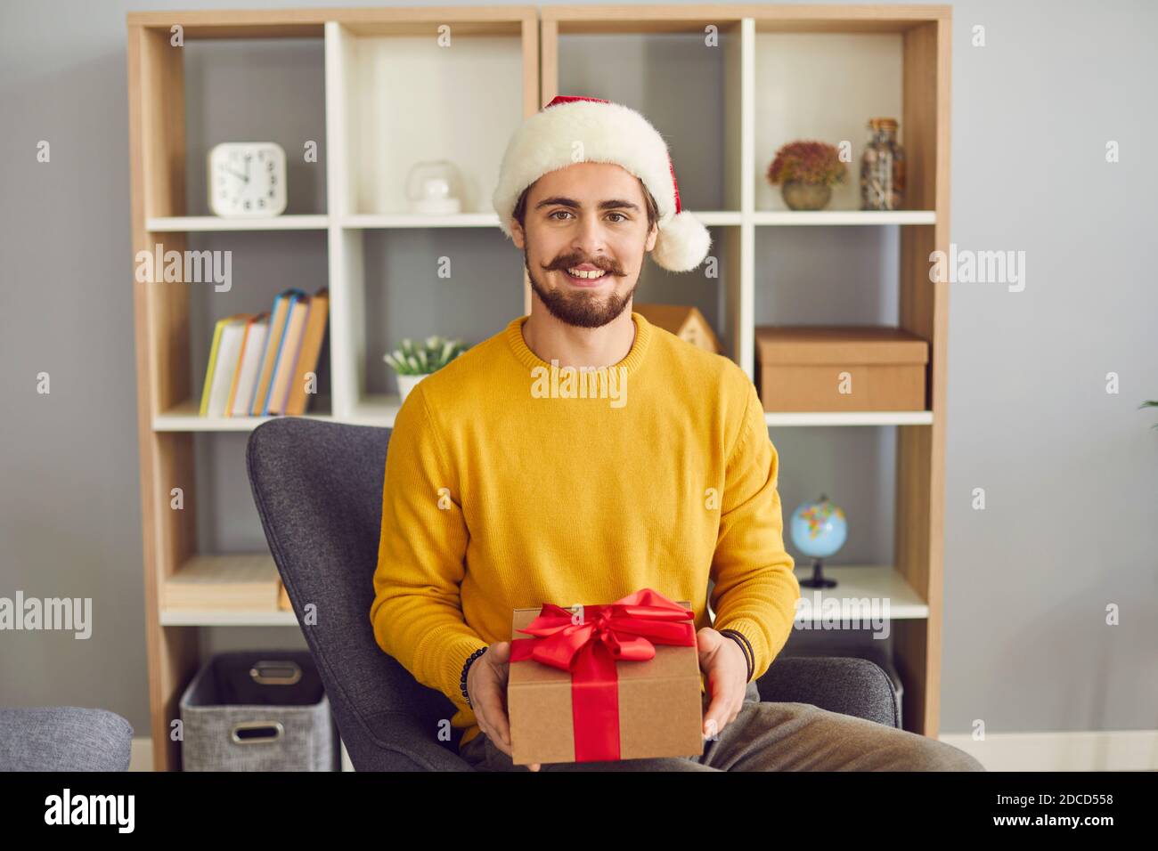 Giovane uomo positivo nel cappello di Satna di Natale che tiene la vacanza presente nelle mani Foto Stock
