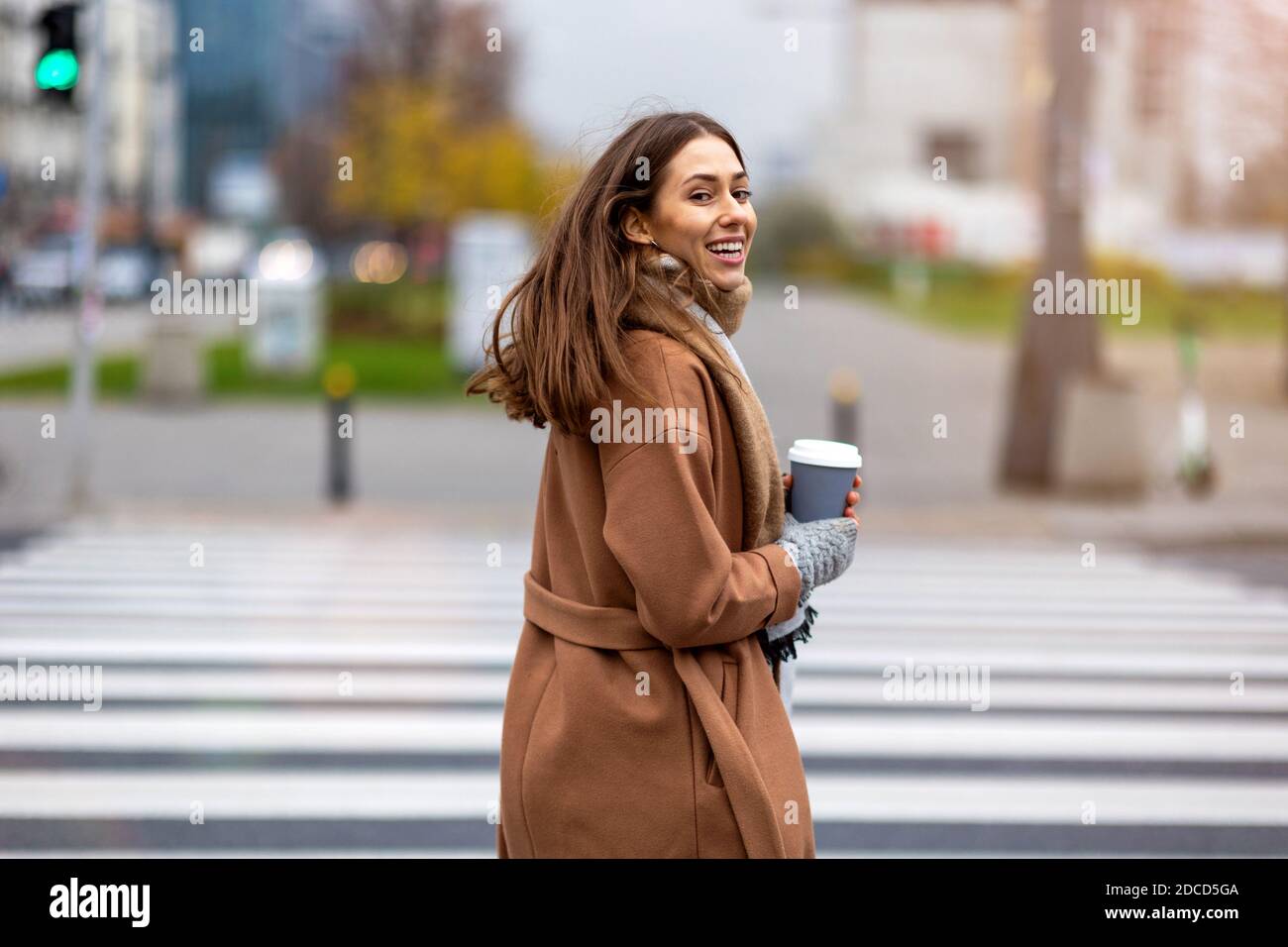 Giovane donna che cammina sulla strada della città tenendo la tazza di caffè Foto Stock