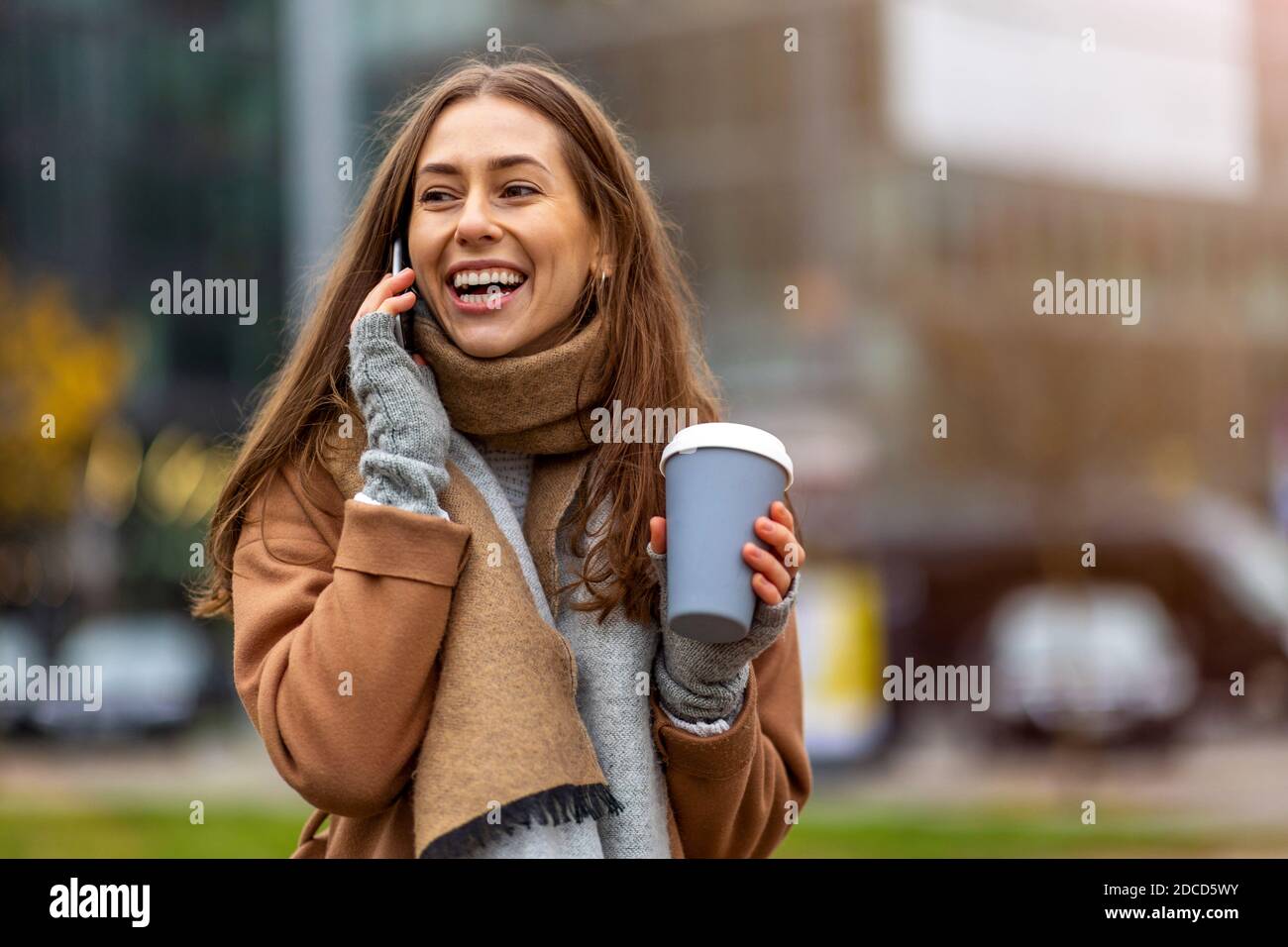Giovane donna sorridente con smartphone e tazza da caffè all'aperto in ambiente urbano Foto Stock