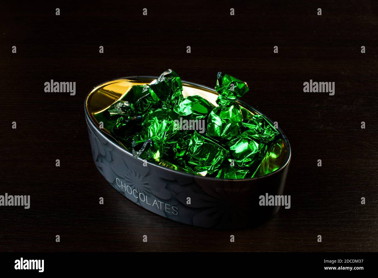 scatola con caramella in involucri di lamina verde su sfondo nero. Foto Stock