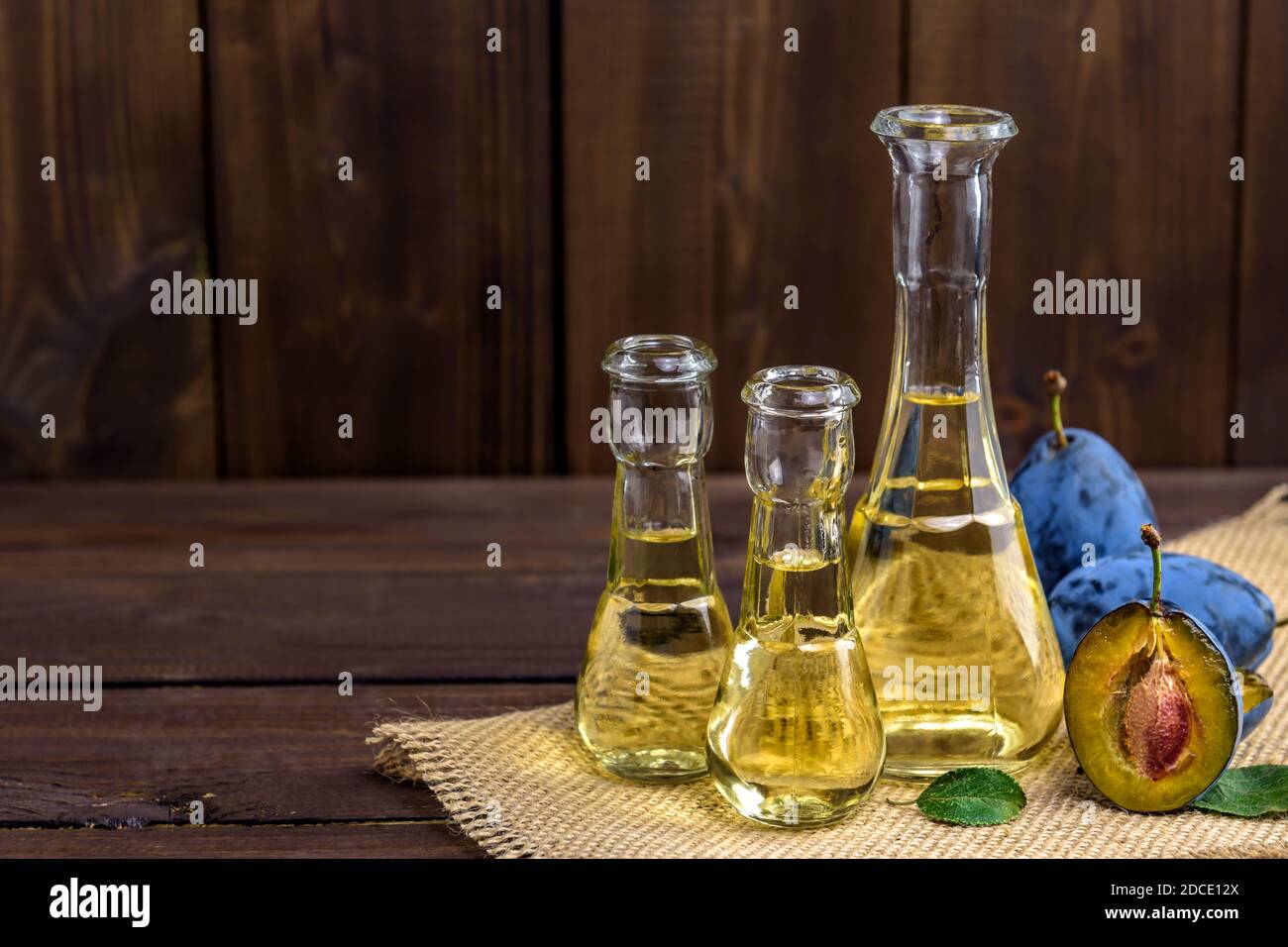 Brandy di prugne o schnapps in piccole bottiglie di vetro con prugne fresche e gustose su un tavolo di legno con spazio di copia per il testo. Messa a fuoco selettiva. Foto Stock