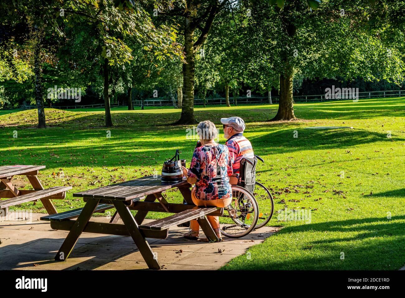 Warrington/Cheshire/UK 21/09/2020 pensionati, moglie che si prende cura del marito disabile seduto su una panchina del parco e rilassante al sole Foto Stock