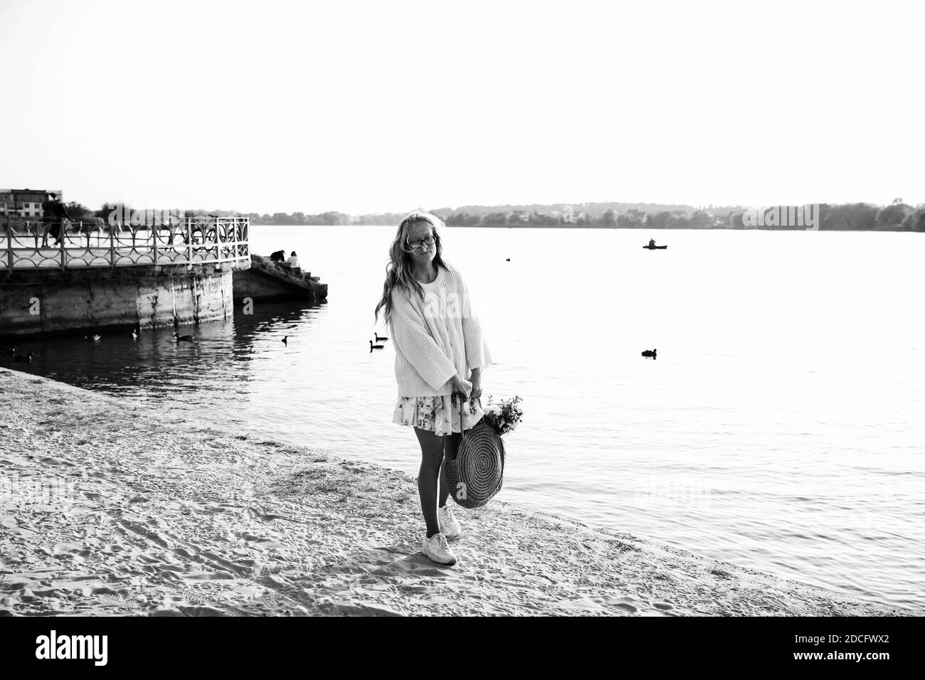 Questa foto mostra una giovane bionda che cammina la spiaggia in un abito e maglione con fiori su una giornata di sole Foto Stock