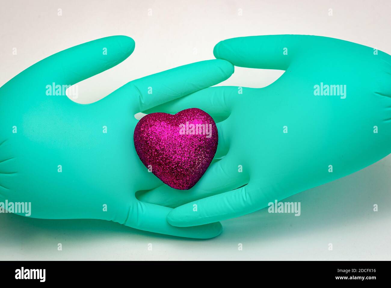 Un paio di guanti medici verdi sono intertwined dita e. tenere un cuore scarlatto Foto Stock