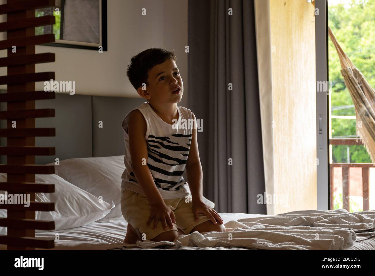 Bambino rilassato guardando la TV in camera d'albergo con sua madre sdraiata in un'amaca sullo sfondo. Foto Stock