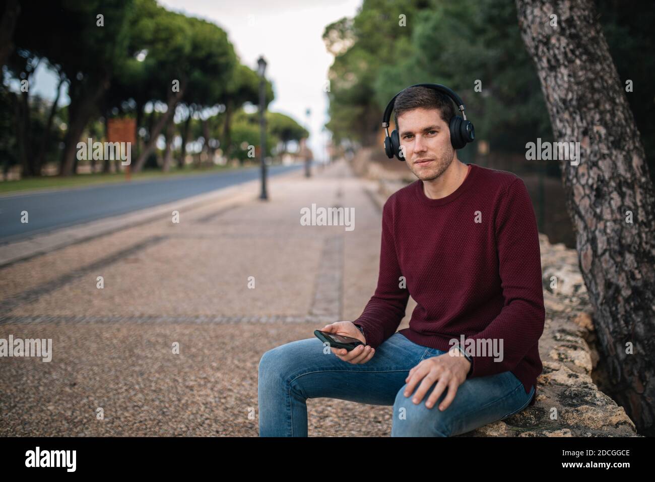 Ragazzo che ascolta la musica con caschi wireless rivolti verso la fotocamera con un gilet rosso. Foto Stock