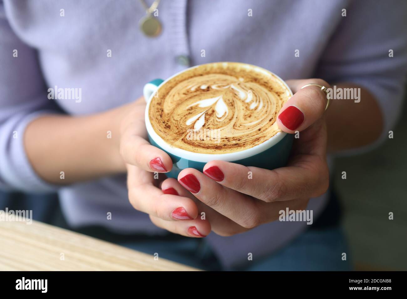 Donna che tiene un caffè latte cappuccino con un design a cuore nella schiuma. Le mani femminili che tengono una tazza di caffè Foto Stock