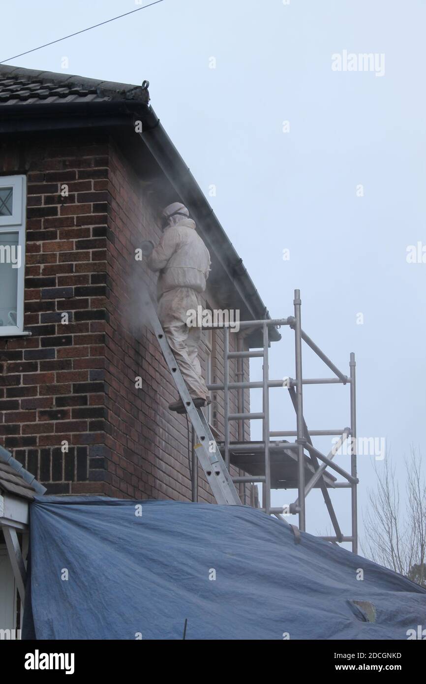 Uomo su impalcature macinando via vecchio indicando su una casa muro con una nuvola di polvere intorno a lui Foto Stock
