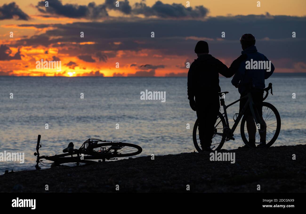 Sagome di un paio di persone (maschi) che illustrano il concetto di famiglia Padre e Figlio, su una spiaggia guardando un tramonto, mentre il sole scende sul mare. Foto Stock