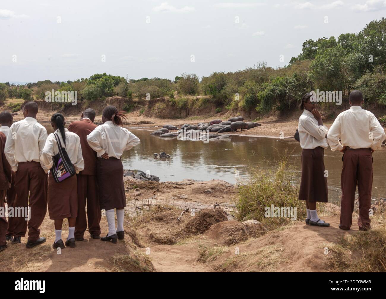 Alunni kenioti che guardano gli ippopotami in un fiume, la provincia di Rift Valley, Maasai Mara, Kenya Foto Stock