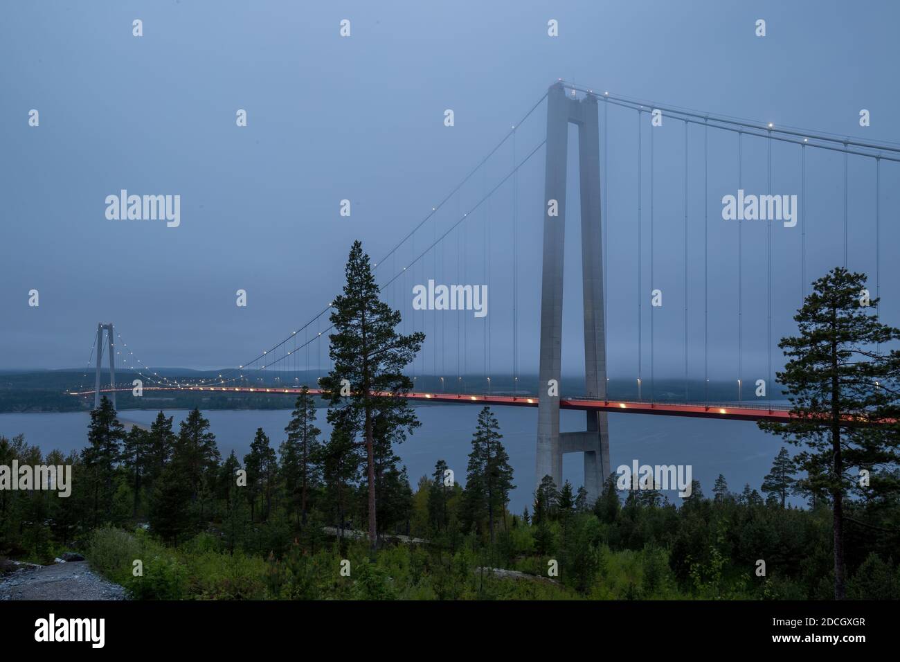 Foto del illuminato Höga Kustenbron, un ponte sospeso che attraversa il fiume Ångermanälven vicino a veda, Svezia, in tarda serata tra le nuvole basse. Foto Stock