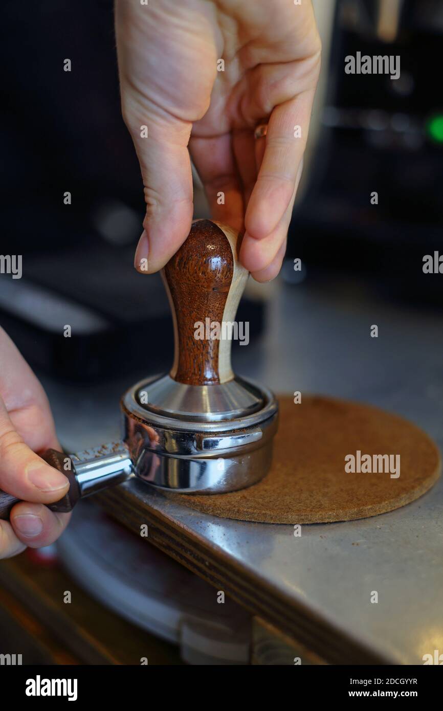 Vista ravvicinata sulle mani, barista maschile che utilizza il antimanomissione per premere il caffè macinato nel portafiltro per preparare una bevanda calda espresso Foto Stock