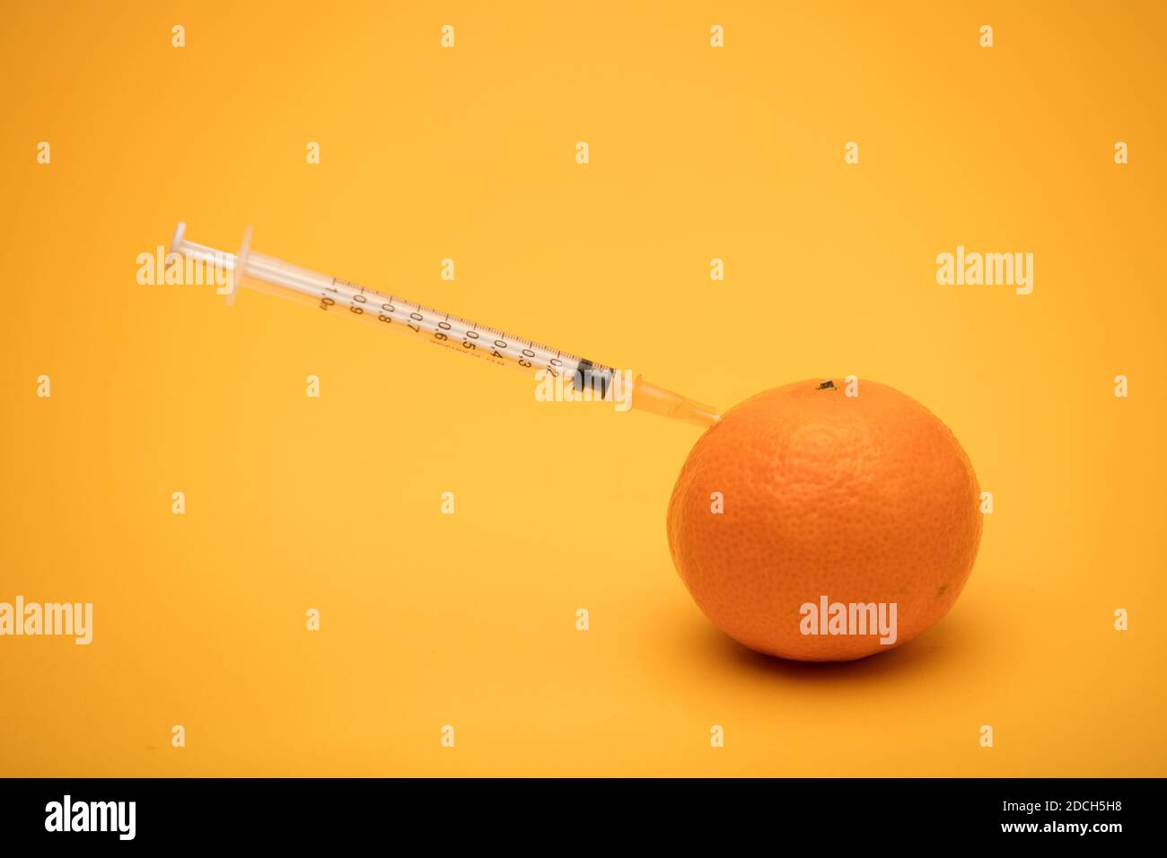 arancione con siringa bloccata, esperimento di modificazione genetica, sfondo arancione Foto Stock