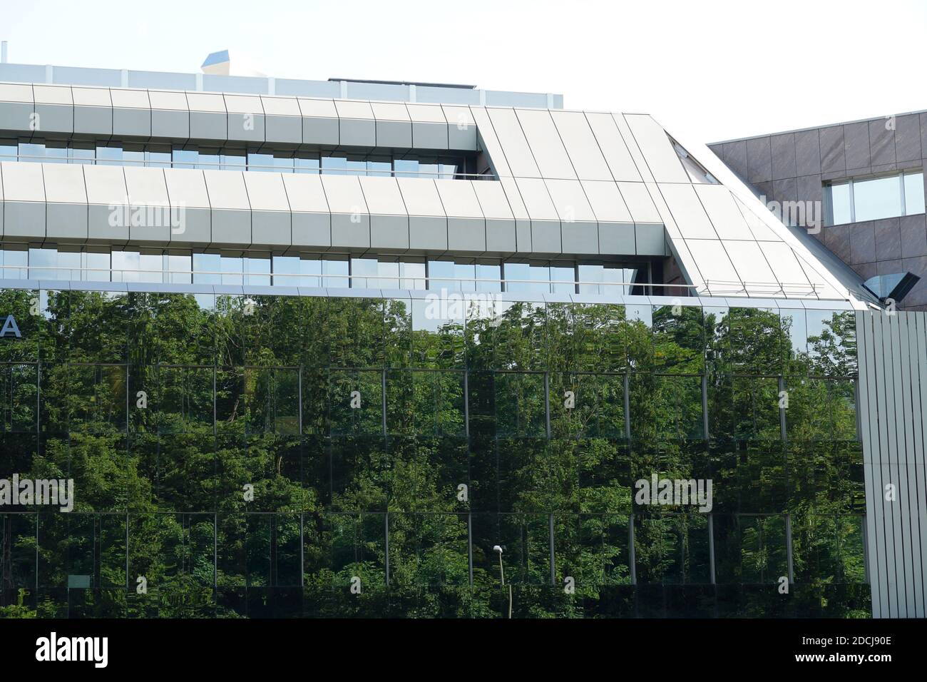 Un edificio moderno con una facciata di vetro. Ci sono alberi che si riflettono nella facciata dando l'impressione o l'illusione di spazio o area verde. Foto Stock