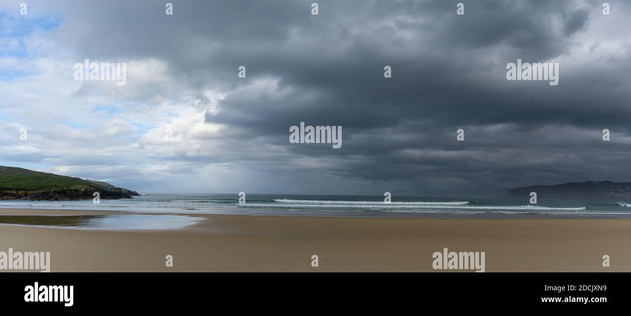 Un panorama di una vuota e grande bella sabbia dorata spiaggia sotto un cielo maltempo Foto Stock