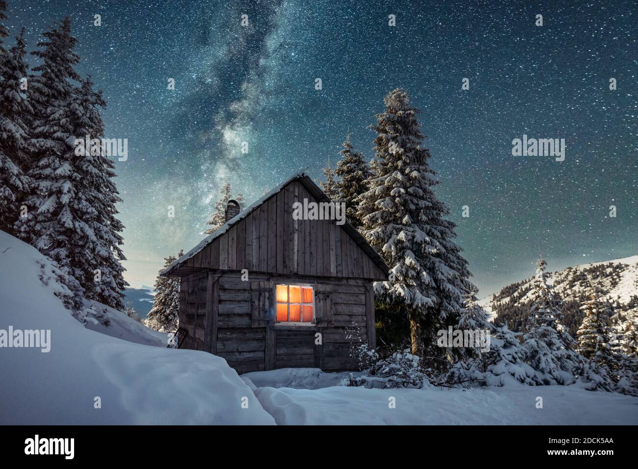 Fantastico paesaggio invernale con casa in legno in montagne innevate. Cielo stellato con Via Lattea e capanna innevata. Vacanza di Natale e concetto di vacanza invernale Foto Stock