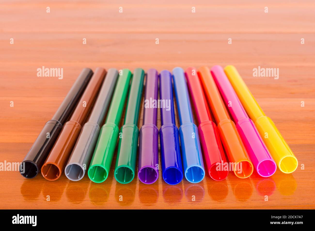 Fila di dodici penne colorate su sfondo di legno marrone. Processo creativo, concetti artistici Foto Stock