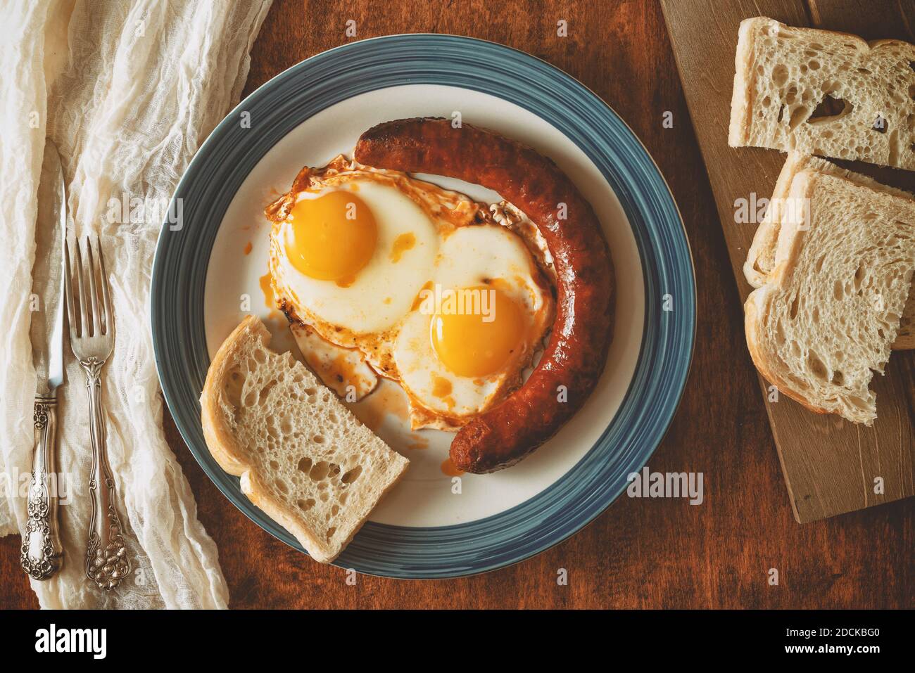 Uova fritte, salsiccia e pane su un piatto da vicino su sfondo di legno, piatto Foto Stock