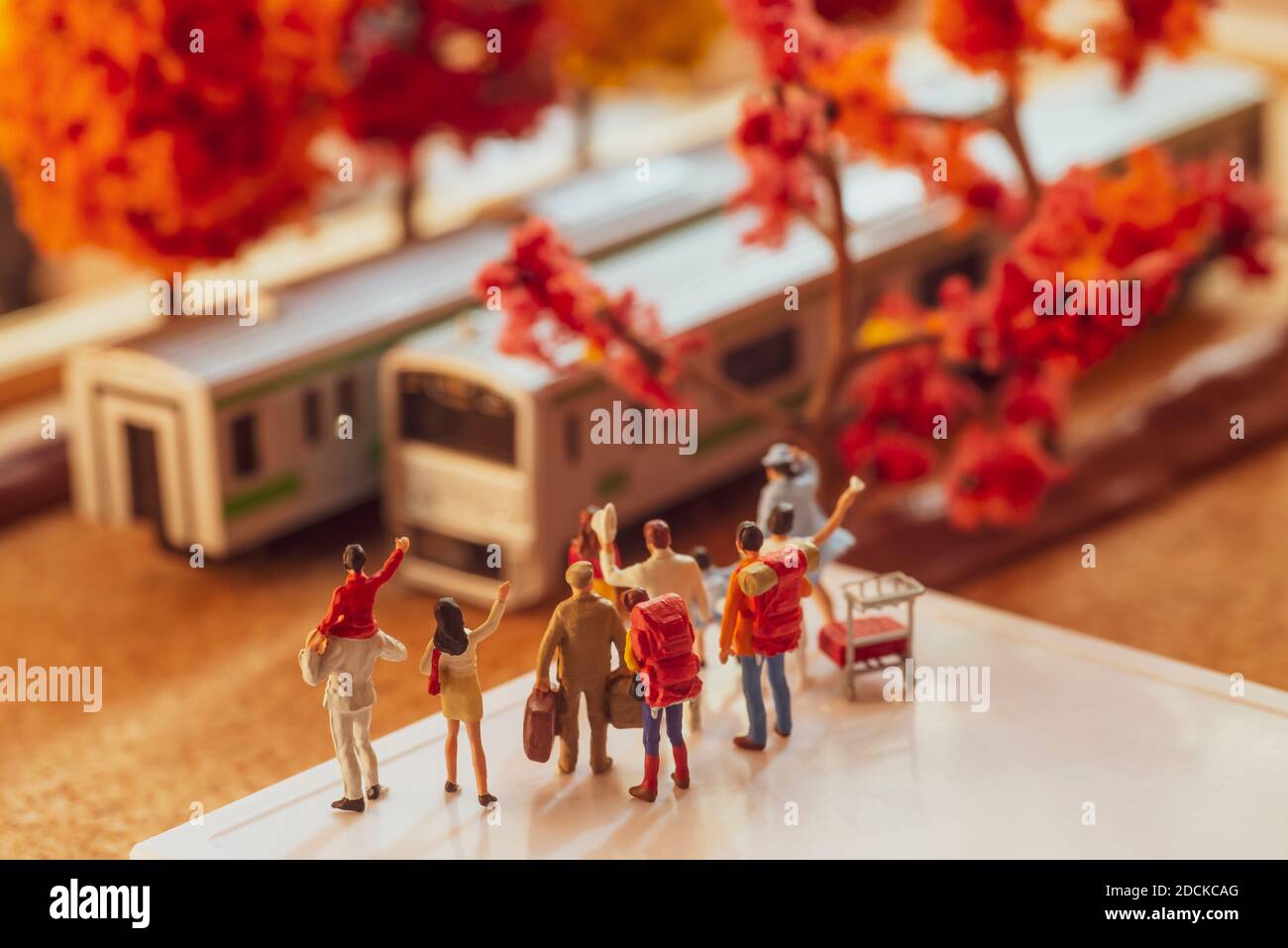 Figurine giocattolo in miniatura di un gruppo di passangers in attesa o in onda a un treno su una piattaforma in autunno o stagione autunnale concetto - filtro tono caldo applicato. Foto Stock