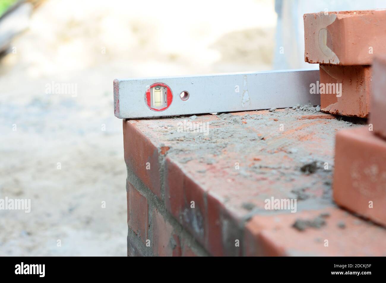 Un primo piano su un livello di sprit usato per livellare i corsi di mattone d'angolo su un letto di mortaio mentre murano il muro della casa. Foto Stock