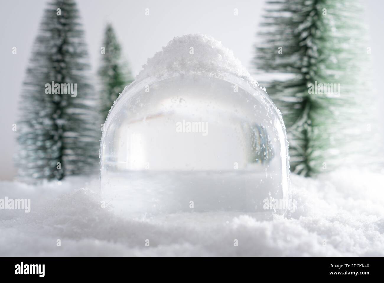 Primo piano di un globo di neve vuoto e isolato coperto di neve in piedi nel mezzo di una foresta finta. Concetto di prevenzione del coronavirus per questo Foto Stock