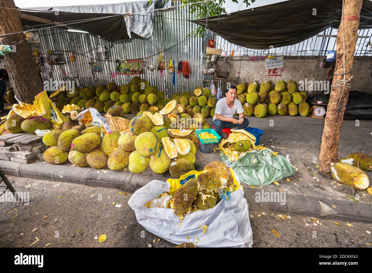 Bangkok, Thailandia - 7 dicembre 2019: Un venditore di frutta di strada siede tra il jackfruit di miele crudo sul mercato di strada locale a Bangkok, Thailandia. Foto Stock