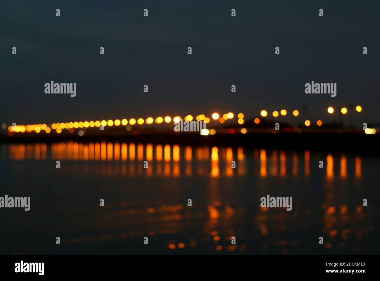 Ponte di mare offuscato astratto di notte con i riflessi di Illuminazione sul mare Foto Stock