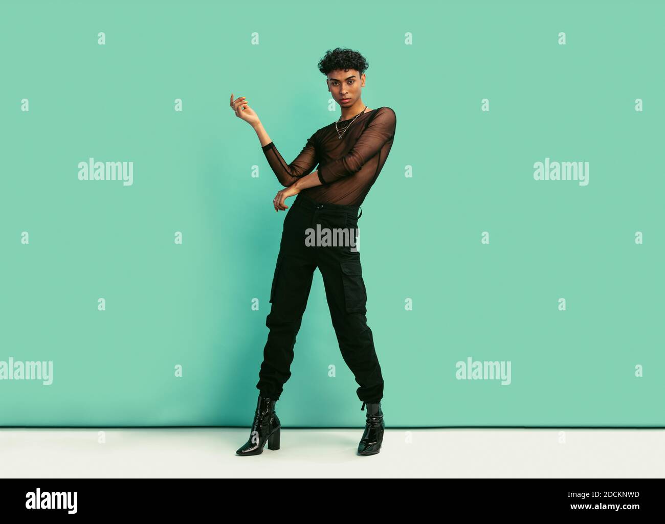 Tutta la lunghezza di un giovane con abiti da donna in posa in studio con espressione. Uomo gay che indossa t-shirt in mesh nera, jeans e tacchi alti guardando Foto Stock