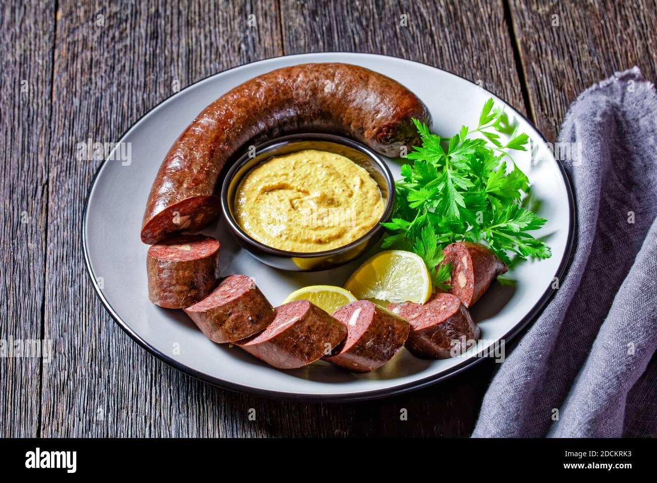 Blutwurst tedesco o salsiccia di sangue tedesco affettato e servito su un piatto con prezzemolo, senape e spicchi di limone serviti su un tavolo di legno, vista dall'alto, vicino Foto Stock
