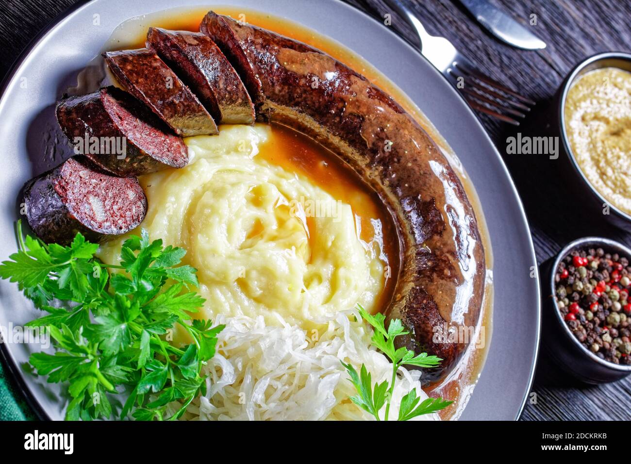 Cibo tedesco: Blutwurst o salsiccia di sangue servita su un piatto con crauti, purè di prezzemolo di patate, senape, e peppercorn su un tavolo di legno scuro, top Foto Stock