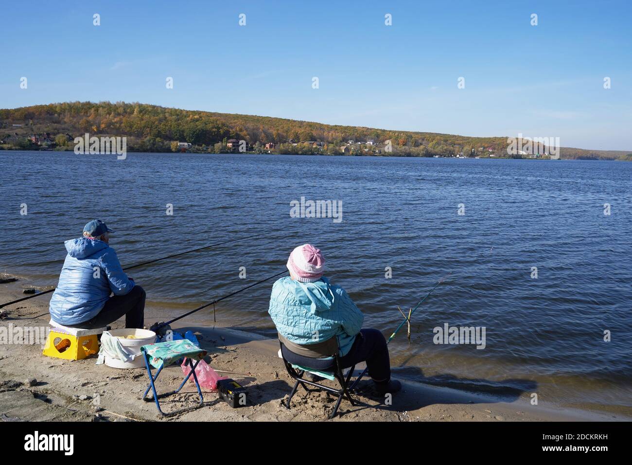 Due persone anziane si siedono sulla riva del fiume con canne da pesca e pesca Foto Stock