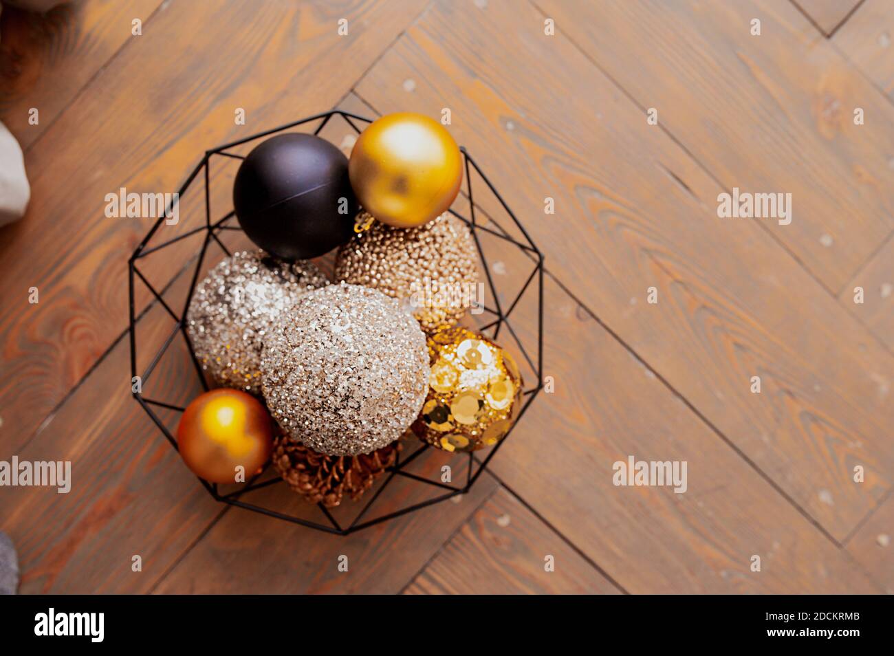 palline dorate, beige e nere lucide per decorazioni natalizie in un cesto nero metallico su una copertina di legno. Carta vacanza, fuoco selettivo Foto Stock