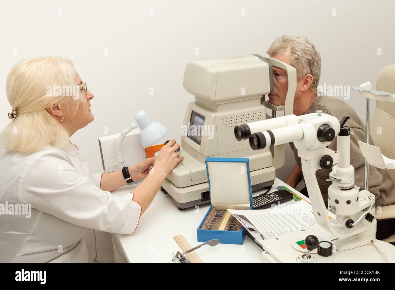 Il medico oftalmologo controlla la vista di un paziente anziano sul rifrattometro moderno Foto Stock